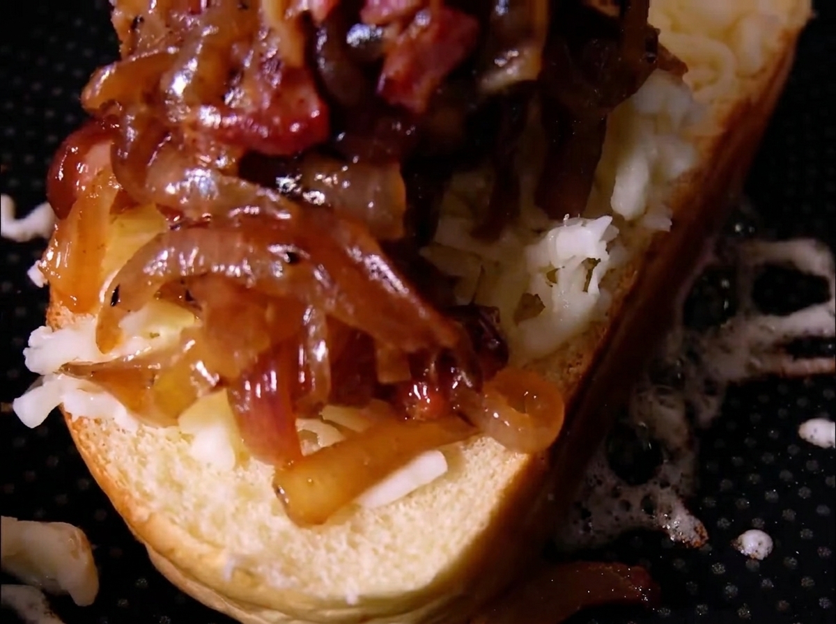 Un généreux tas doignons caramélisés et de morceaux de bacon reposant sur du fromage râpé sur une tranche de pain.