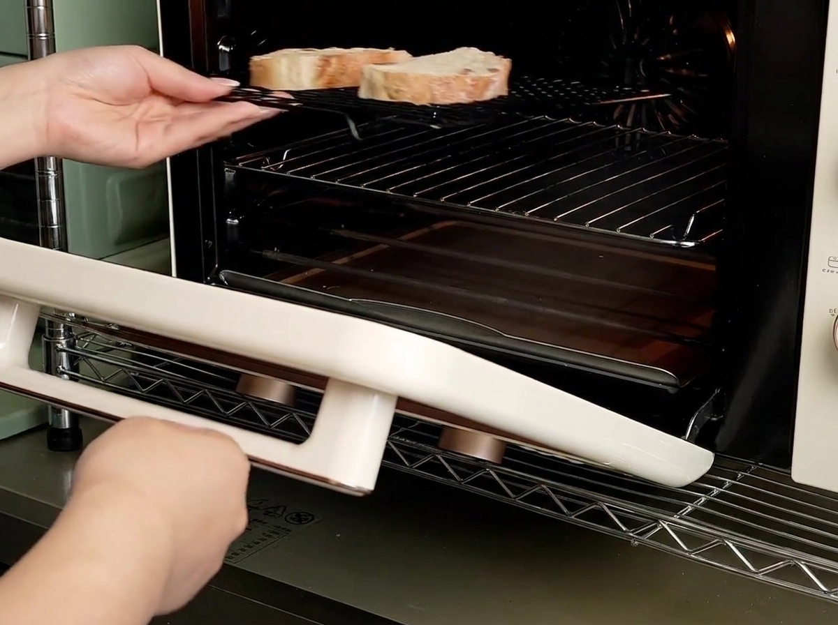 Des mains glissant une grille contenant deux tranches de pain dans un petit four de comptoir.