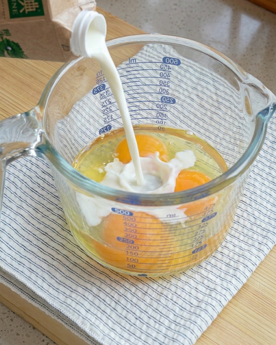Du lait versé dans un grand verre mesureur contenant trois œufs crus cassés.