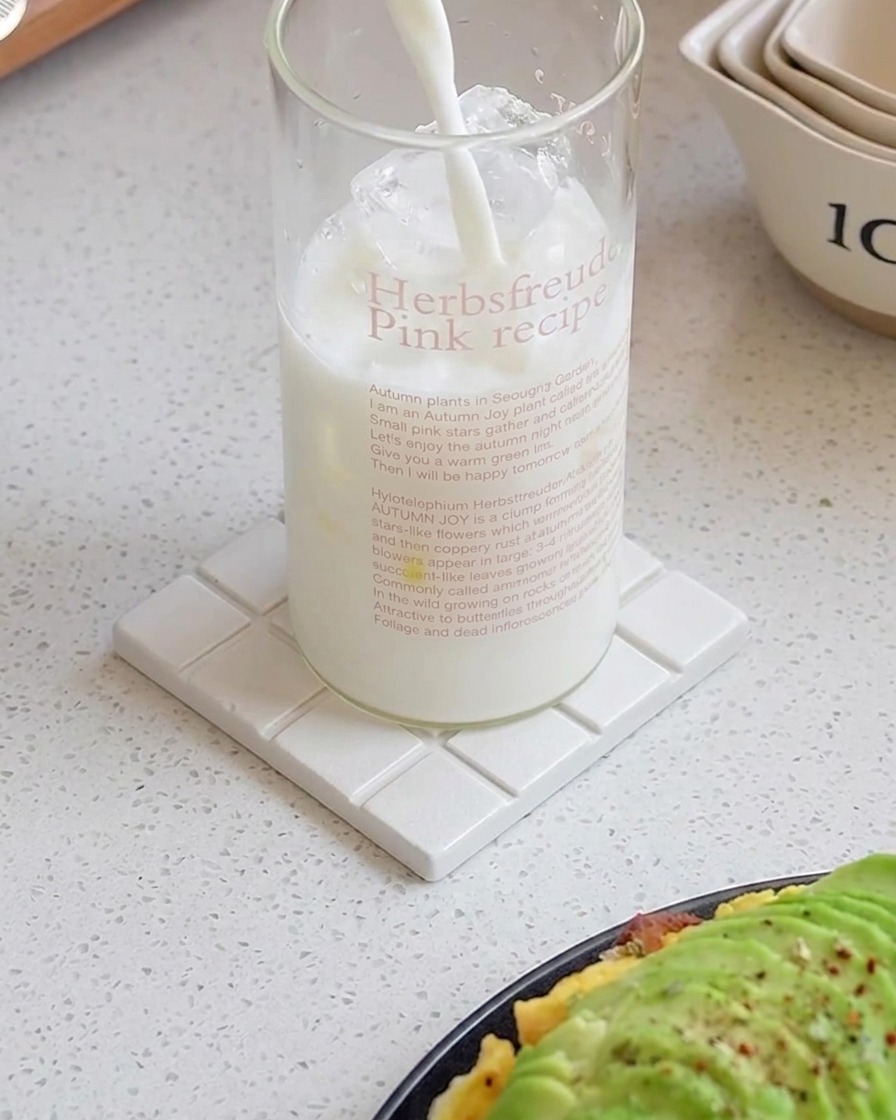 Du lait versé dans un grand verre rempli de glaçons sur un sous-verre blanc.