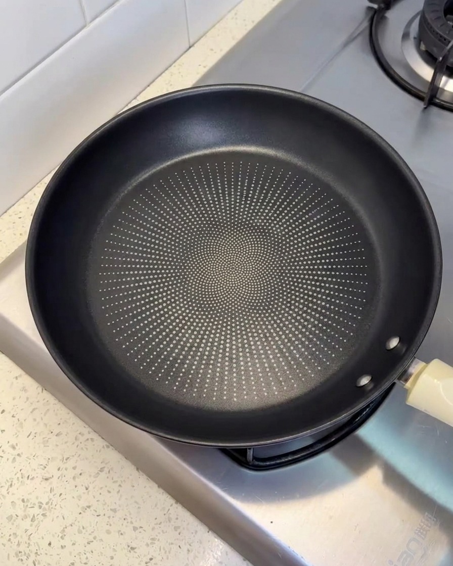 Une poêle antiadhésive noire posée sur un feu de cuisson, légèrement huilée.