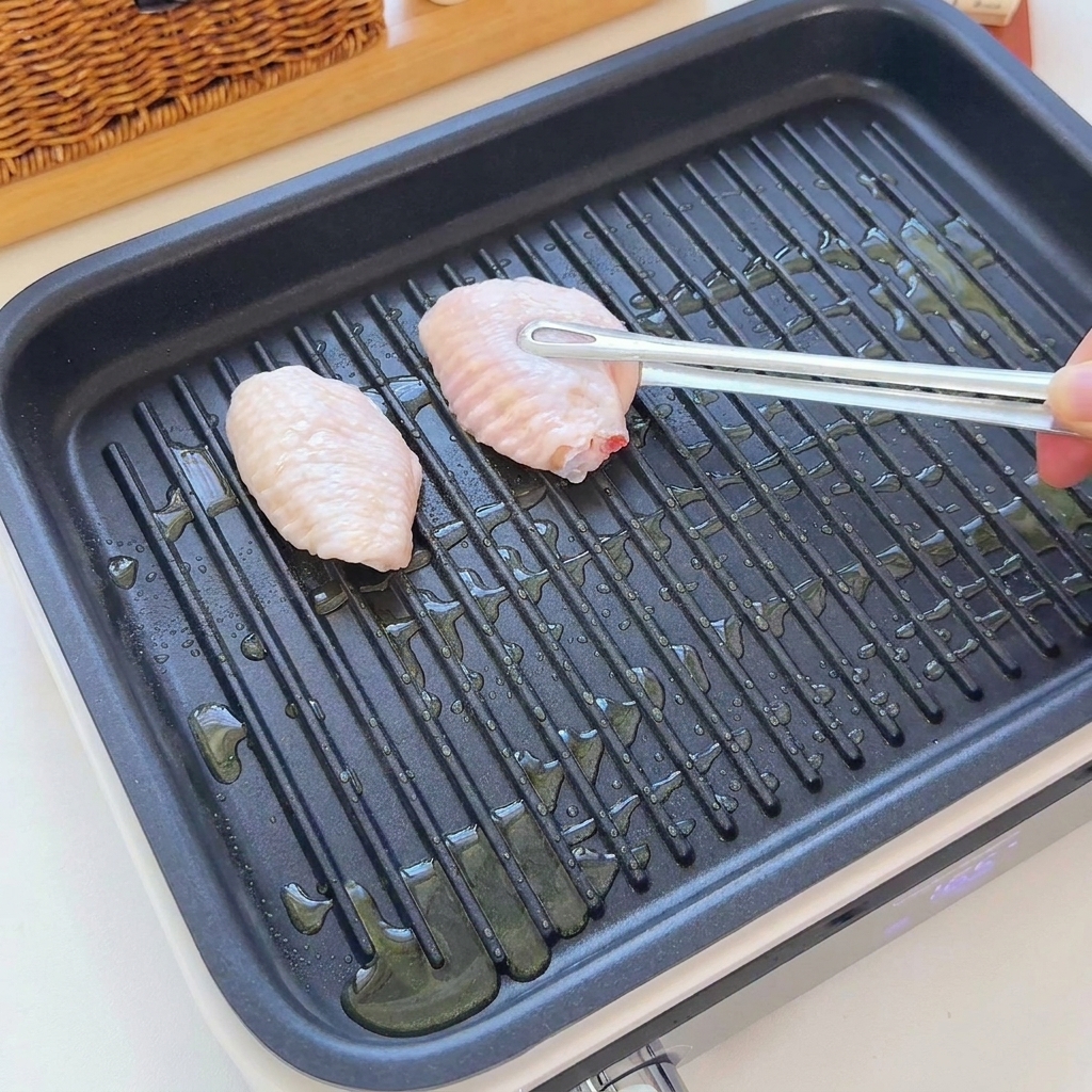 Ailes de poulet crues placées sur un gril nervuré avec de lhuile à laide de pinces.