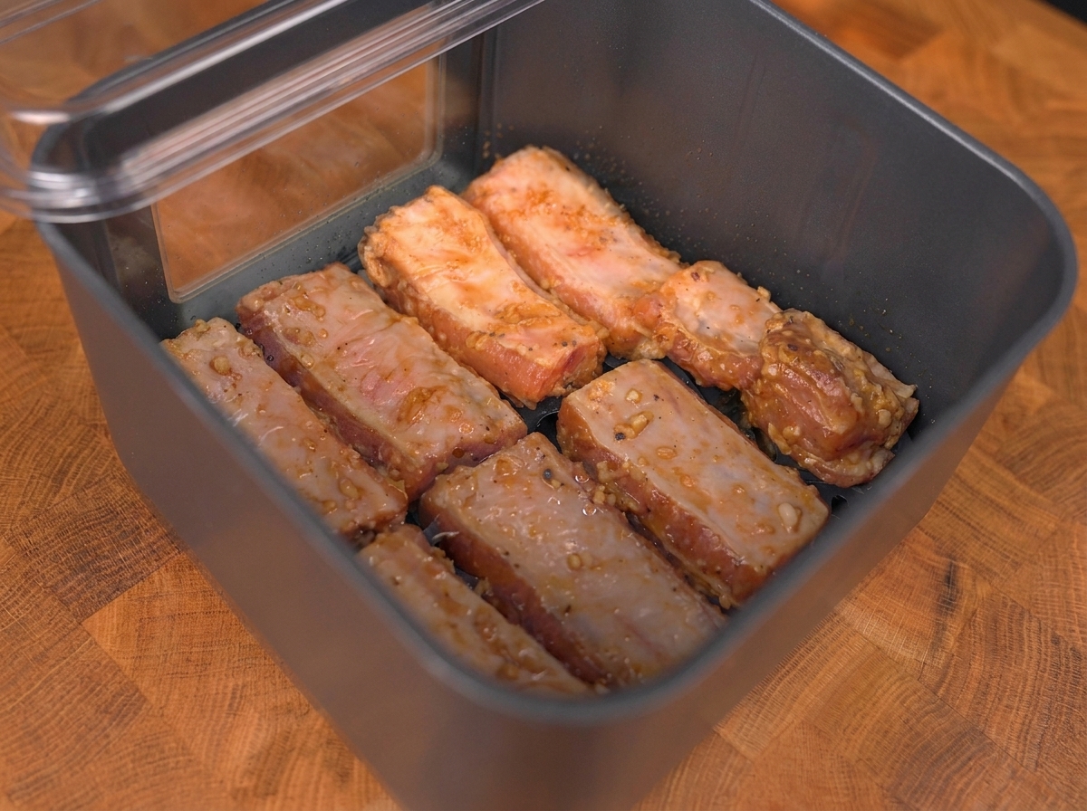 Travers de porc marinés disposés en une seule couche dans le panier de lAir Fryer.