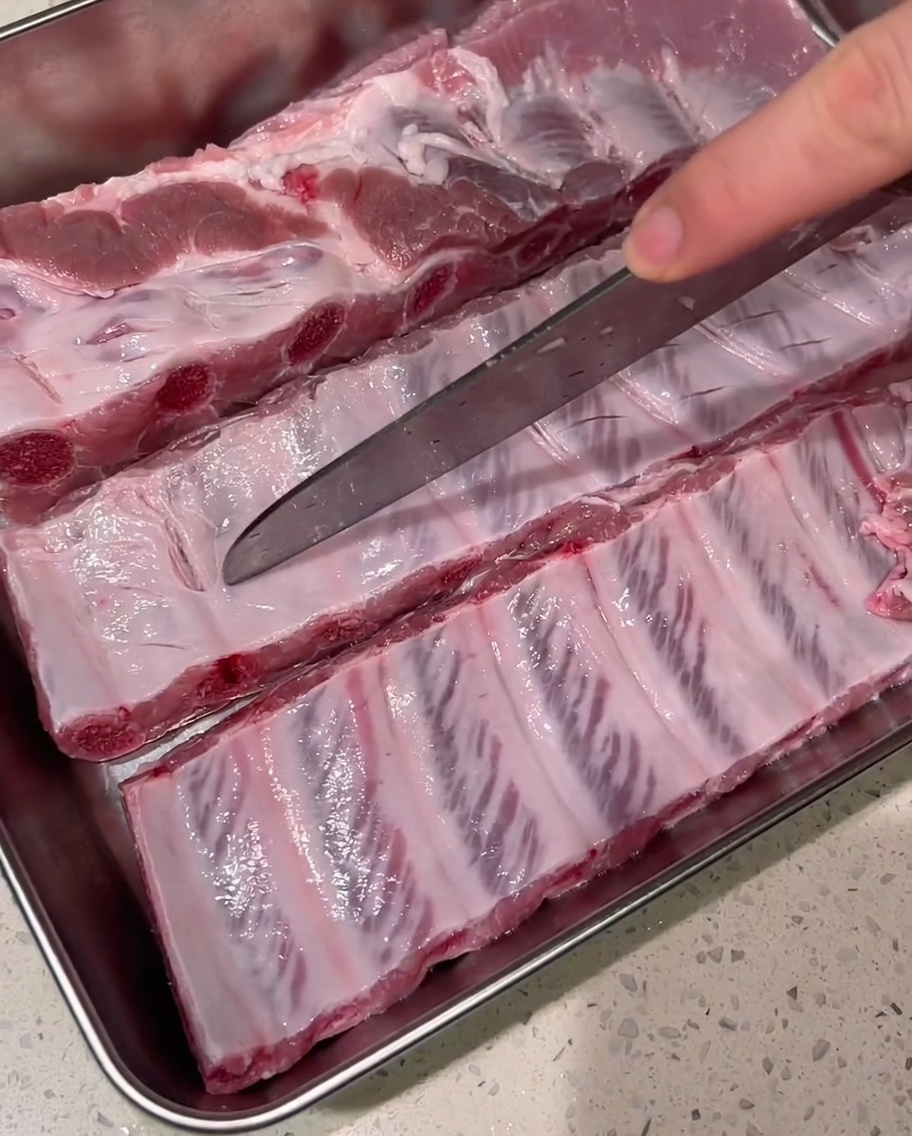 Un couteau bien aiguisé pratiquant des coupes peu profondes sur le fascia de travers de porc crus sur un plateau en métal.