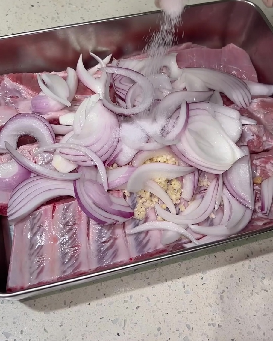 Du sel saupoudré généreusement à la main sur les travers de porc assaisonnés et les oignons.