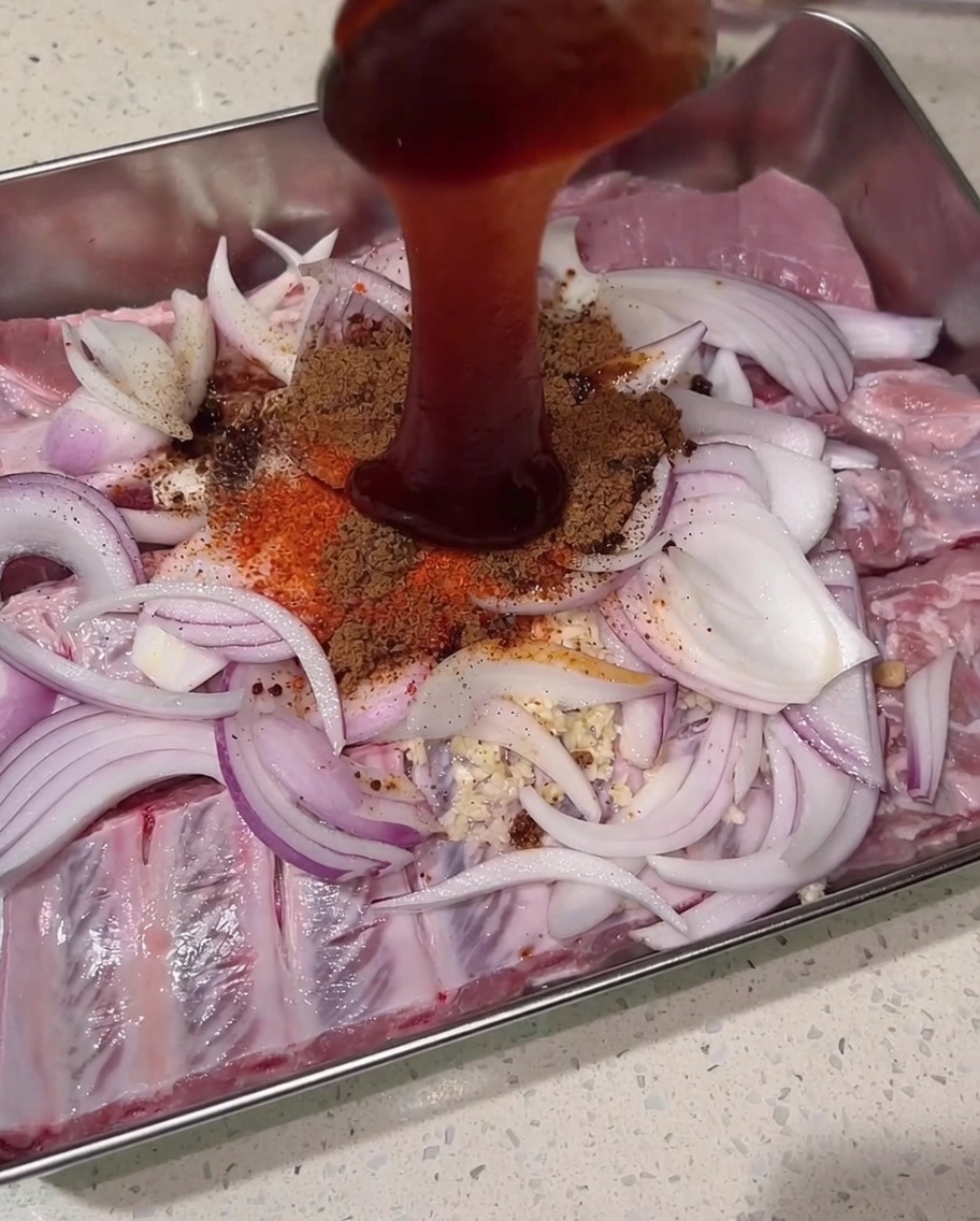 Une sauce char siu épaisse et rouge foncé versée du dessus sur le monticule dépices sèches, de travers de porc crus et doignons.