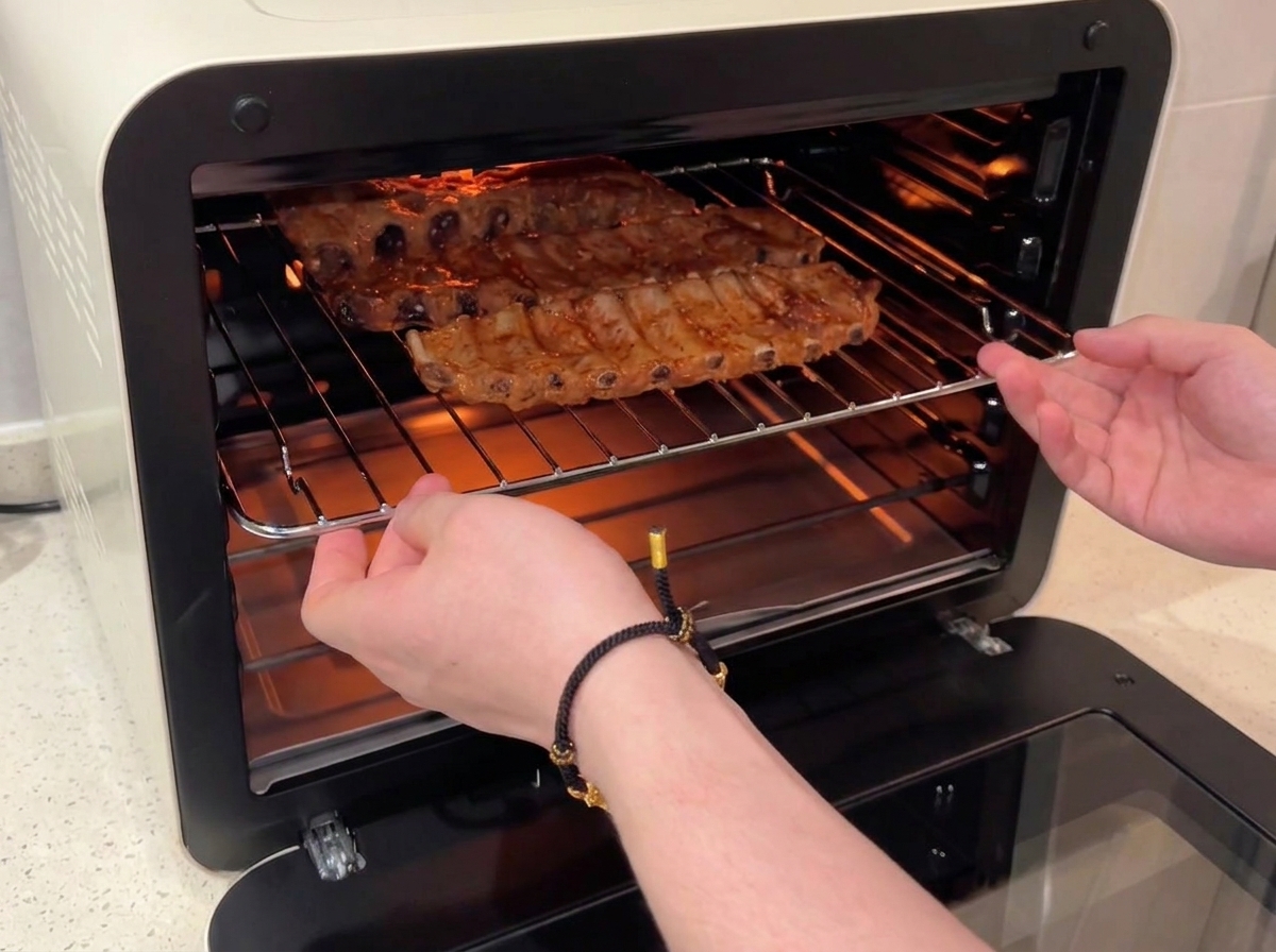 Des mains glissant une grille contenant des travers de porc glacés au miel dans un four à convection allumé.