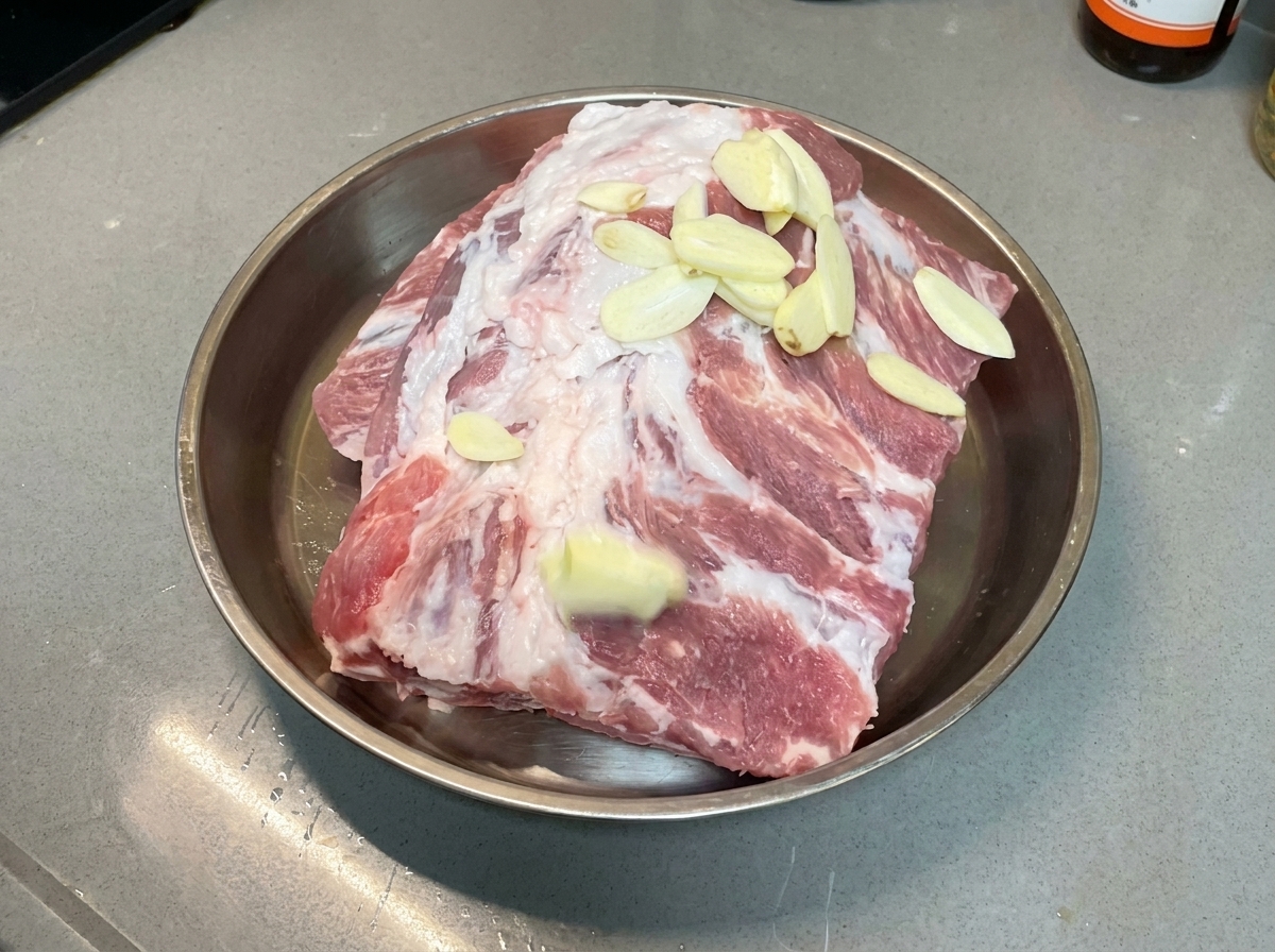 Tranches dail réparties uniformément sur des travers de porc crus reposant dans un plat en métal.