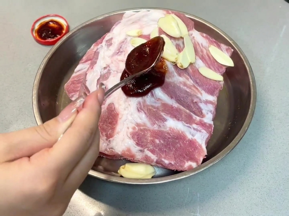 Une cuillerée de sauce char siu foncée versée sur les travers de porc dans un plat en métal.