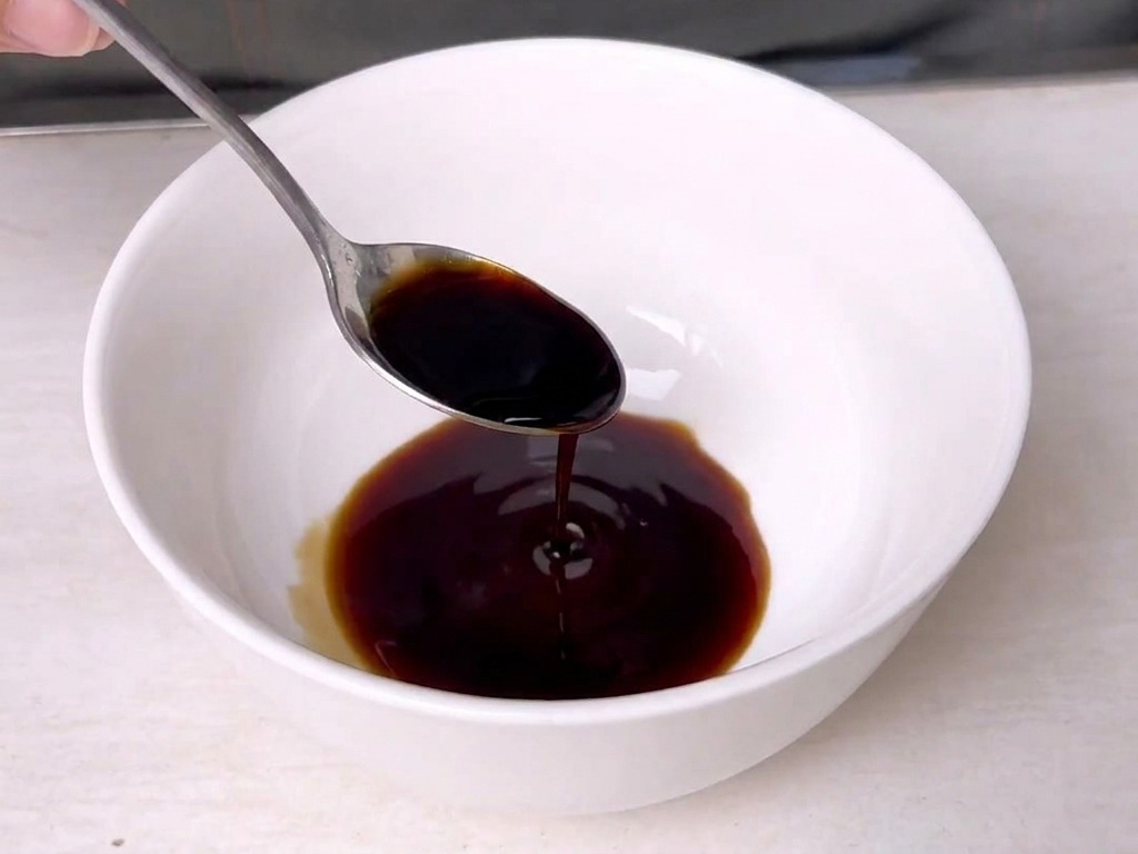 Une cuillère en métal remuant une sauce sombre et riche à lintérieur dun petit bol en céramique blanche.
