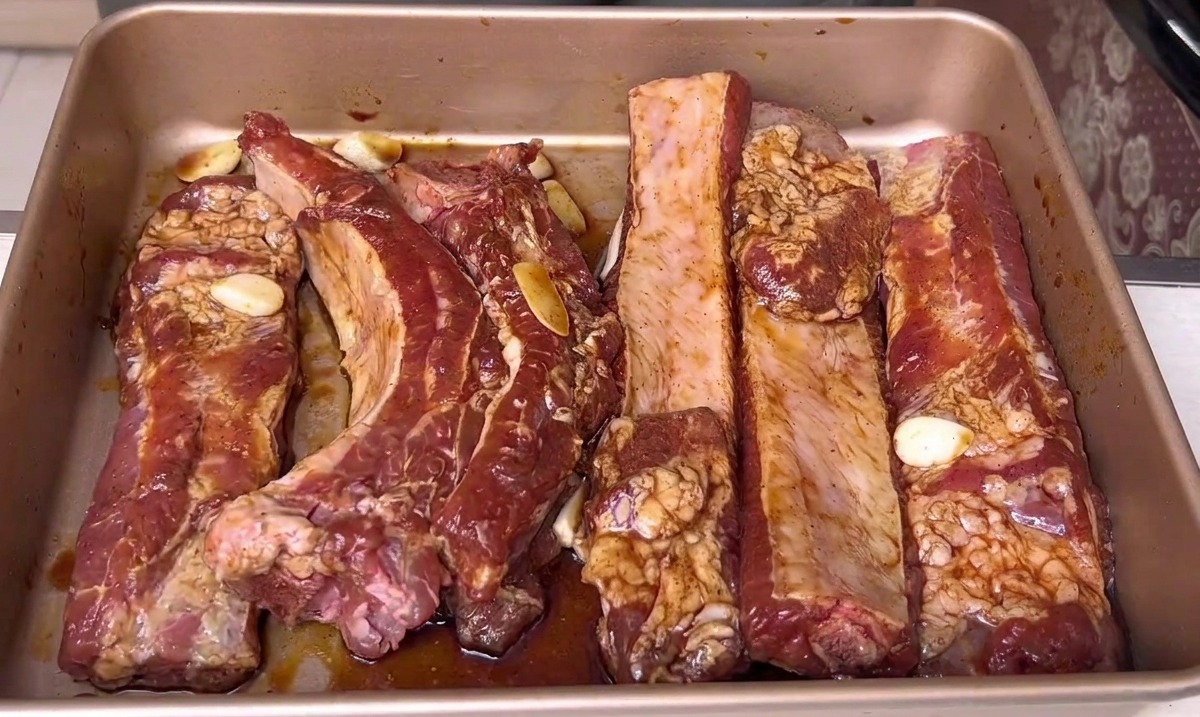 Côtes de porc marinées reposant dans un plateau de cuisson doré, prêtes à être enfournées.