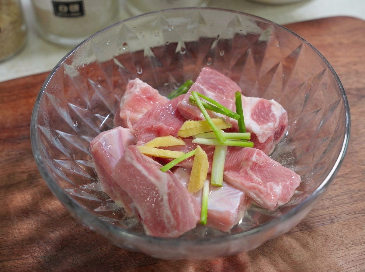 Des tranches de gingembre et des morceaux doignon vert reposant sur des travers de porc dans un bol en verre.