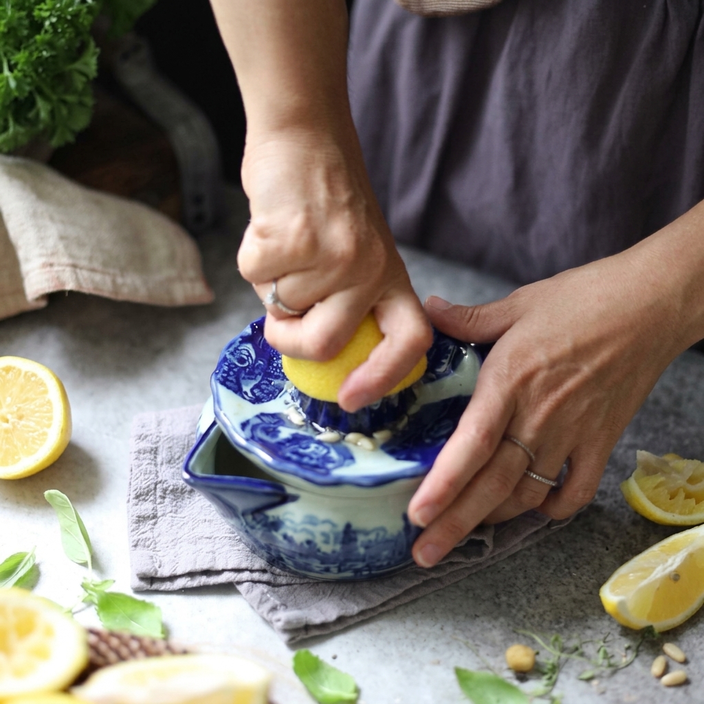 Des mains pressant et tordant un demi-citron sur un ⁠presse-agrumes manuel en céramique bleue et blanche.