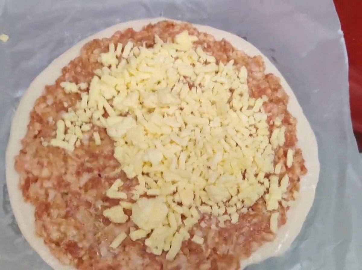 Du fromage jaune râpé empilé sur une couche de viande hachée crue posée sur une galette doignons verts.