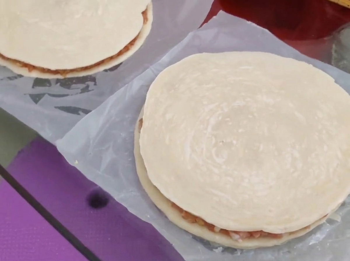 Une seconde galette doignons verts ronde placée par-dessus la garniture de viande et de fromage pour former une tourte fermée.