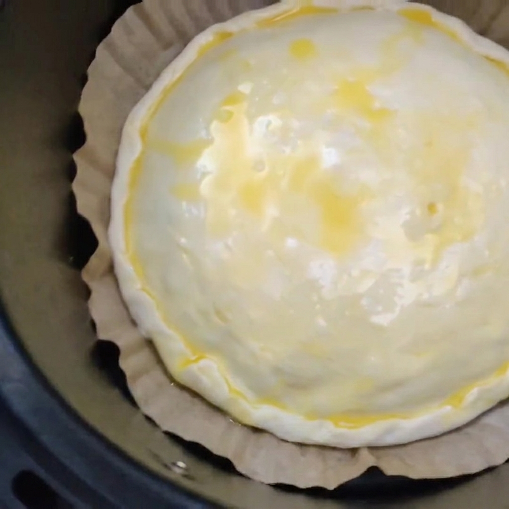 Une tourte crue à la viande et au fromage avec une dorure à lœuf, reposant sur du papier sulfurisé marron à lintérieur du panier noir dune friteuse sans huile.