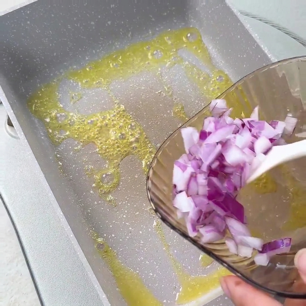 Oignons rouges hachés versés dun bol en verre dans du beurre fondu dans une poêle carrée.