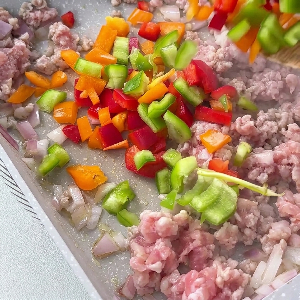 Poivrons rouges, jaunes et verts en dés ajoutés à la poêle avec le mélange de viande.