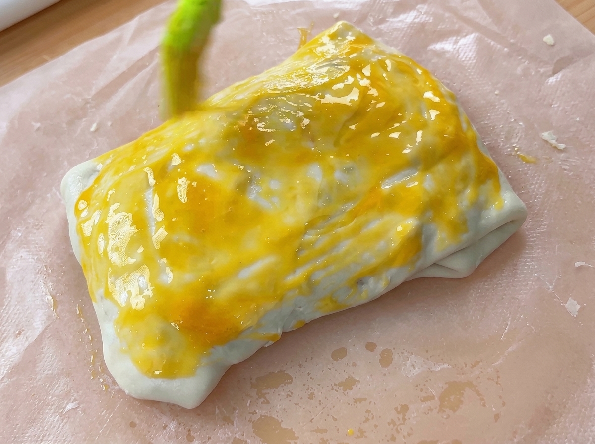 Un pinceau à pâtisserie appliquant une couche de dorure à lœuf jaune vif sur un chausson de pâte plié.
