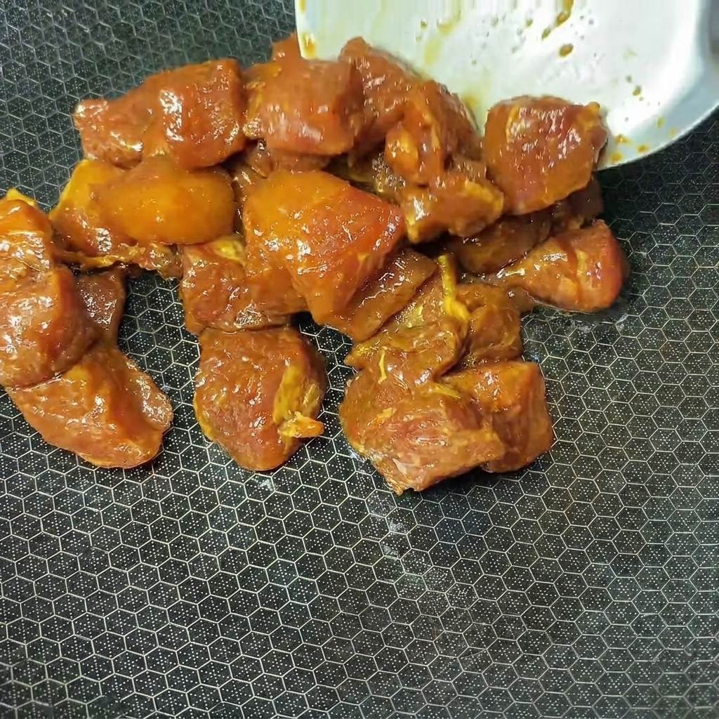 Dés de porc marinés déposés dans un wok très chaud pour la cuisson.