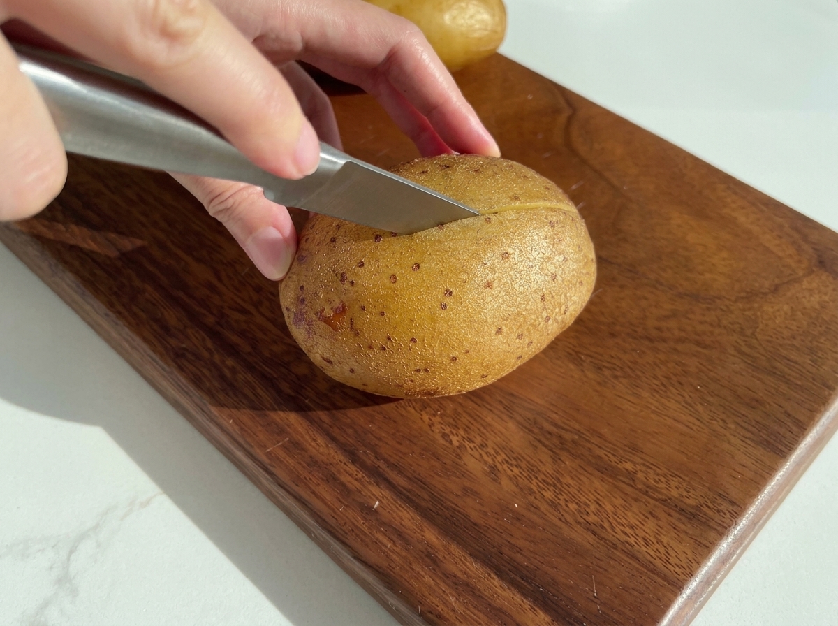 Un couteau coupant une pomme de terre cuite sur une planche à découper en bois.