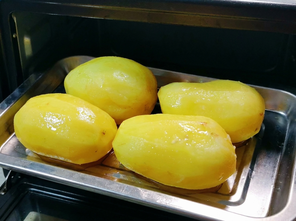Une plaque en métal de pommes de terre entières huilées placée à lintérieur dun petit four noir.