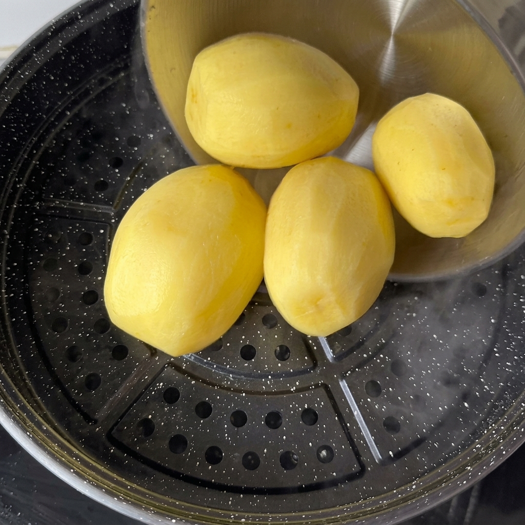 Pommes de terre jaunes épluchées disposées sur un plateau vapeur au-dessus deau bouillante.