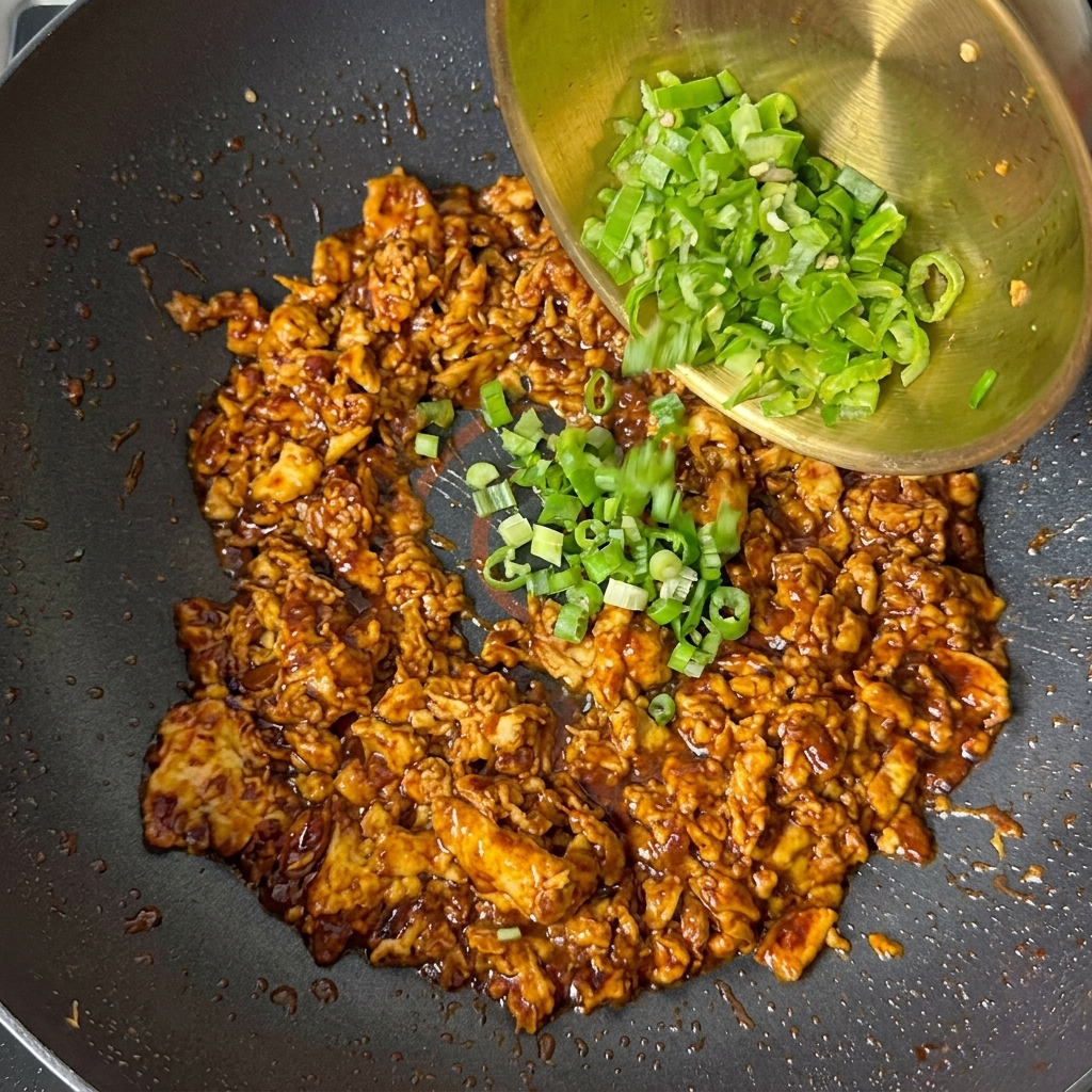 Oignons verts hachés et morceaux de poivron vert versés dun bol doré sur le mélange dœufs cuits.