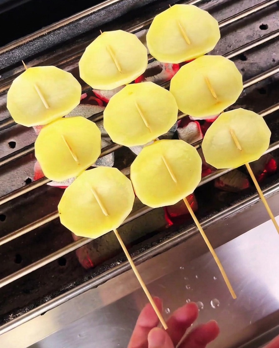 Tranches de pommes de terre pâles sur des brochettes en train de sécher sur un gril à charbon.