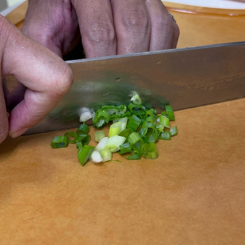 Des oignons verts coupés en petites rondelles avec un couteau sur une planche à découper.