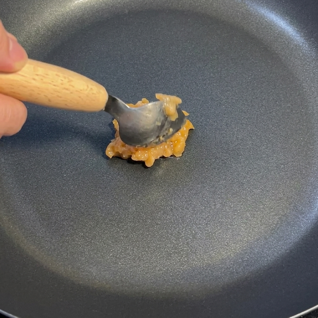 Une cuillère de sauce à lail et au gingembre remuée dans une poêle antiadhésive à feu doux.