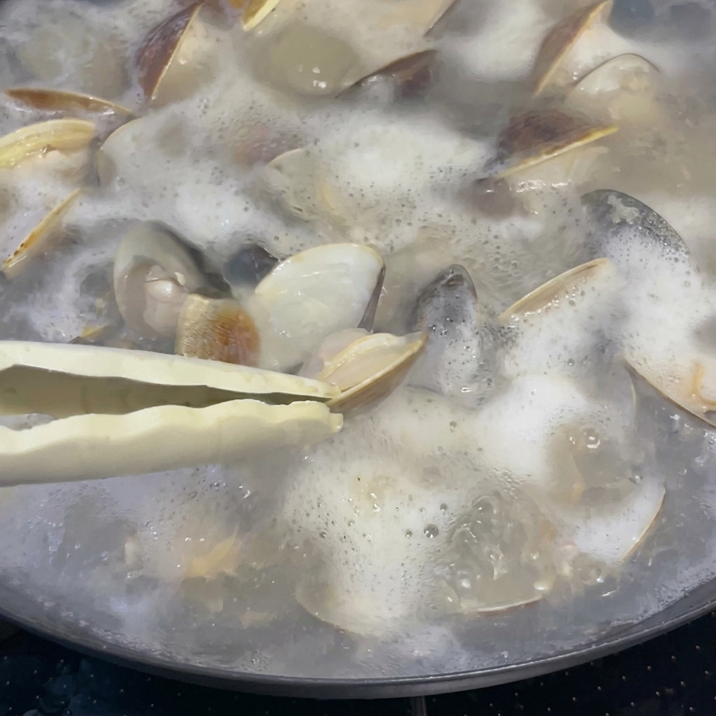 Une cuillère à soupe de vin de riz ajoutée au bouillon frémissant contenant les palourdes.