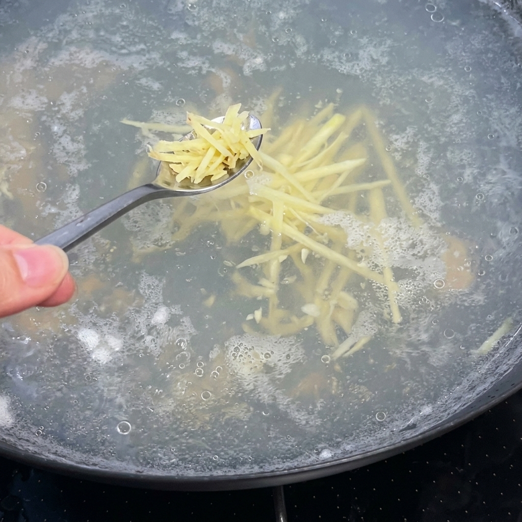 Une cuillerée de gingembre émincé ajoutée dans la casserole de bouillon clair en ébullition.