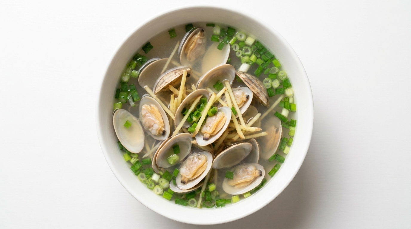 Un bol fumant de soupe de palourdes claires avec ses coquilles ouvertes, parsemée de julienne de gingembre frais et doignons verts ciselés.