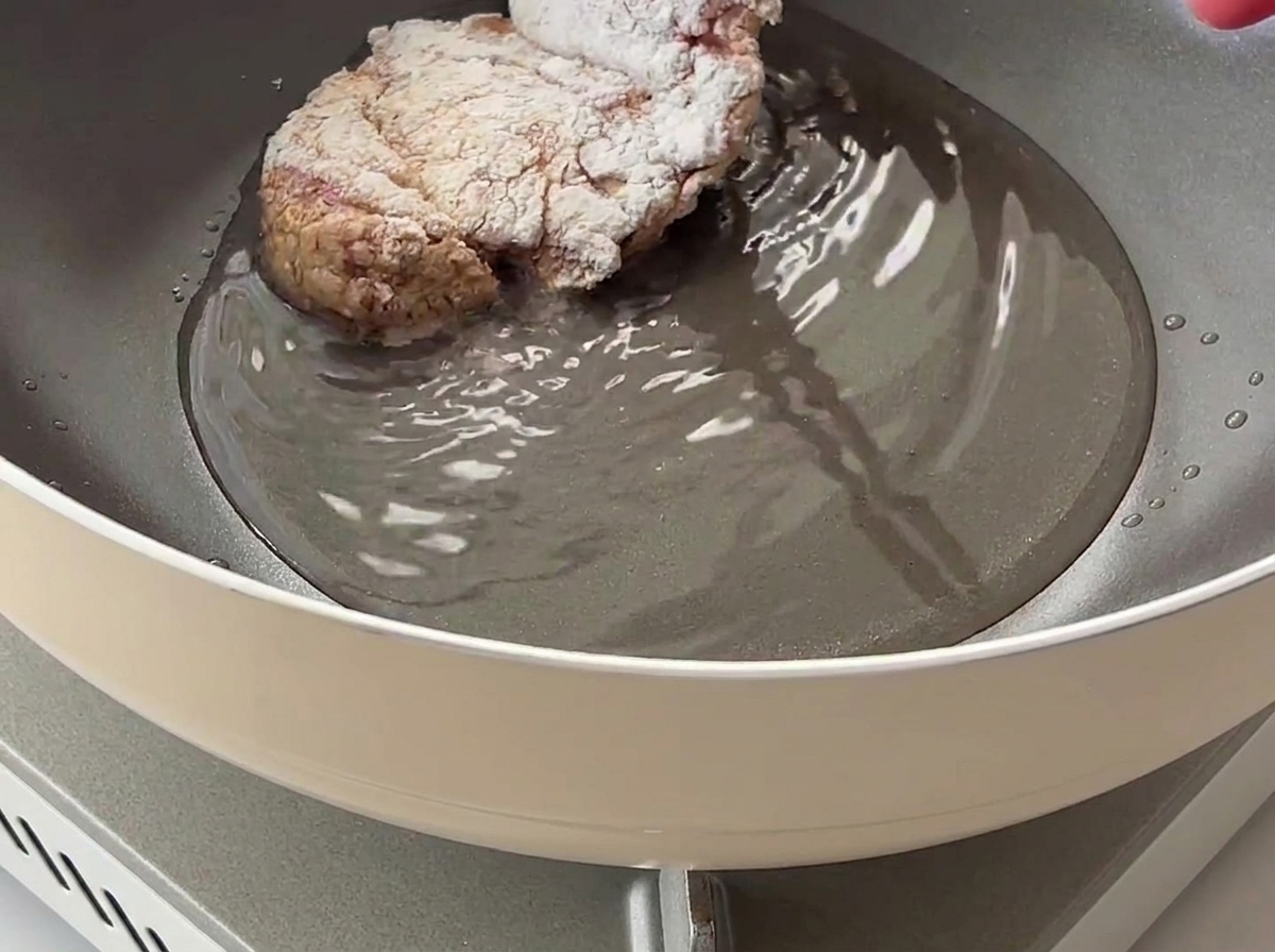 Une cuisse de poulet enrobée de fécule de maïs placée dans une poêle contenant de lhuile de cuisson chaude.