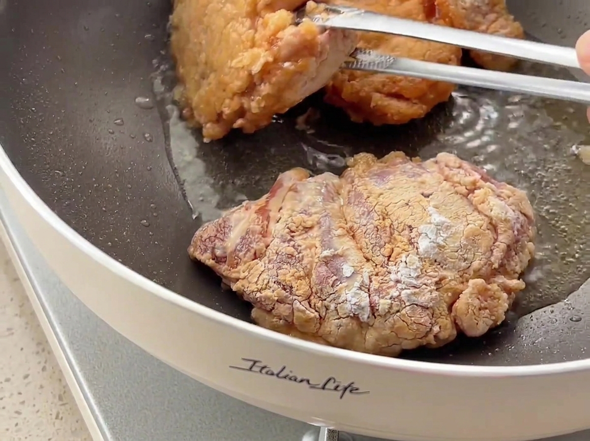 Morceaux de poulet retournés avec des pinces dans une poêle, révélant une croûte dorée et croustillante.