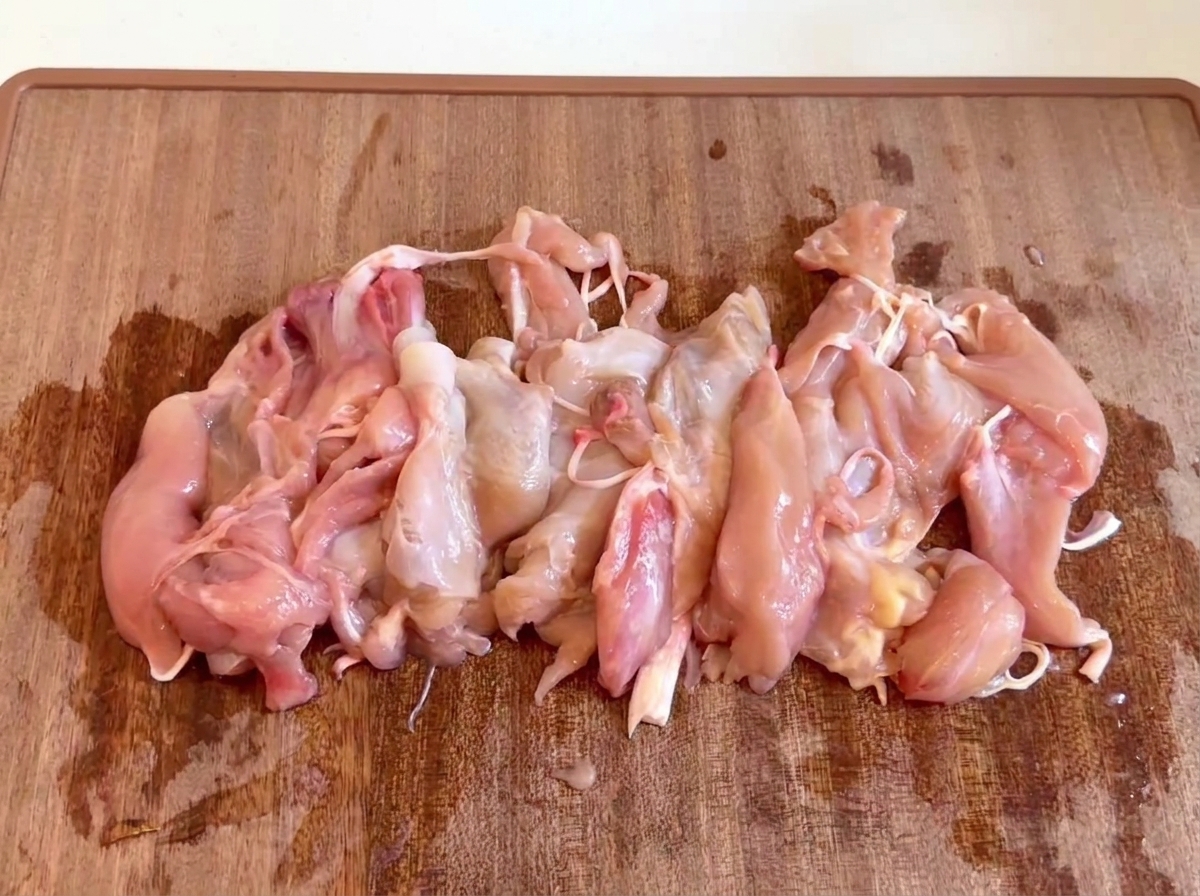 Morceaux de viande de poulet crus et désossés rassemblés sur une planche à découper en bois.