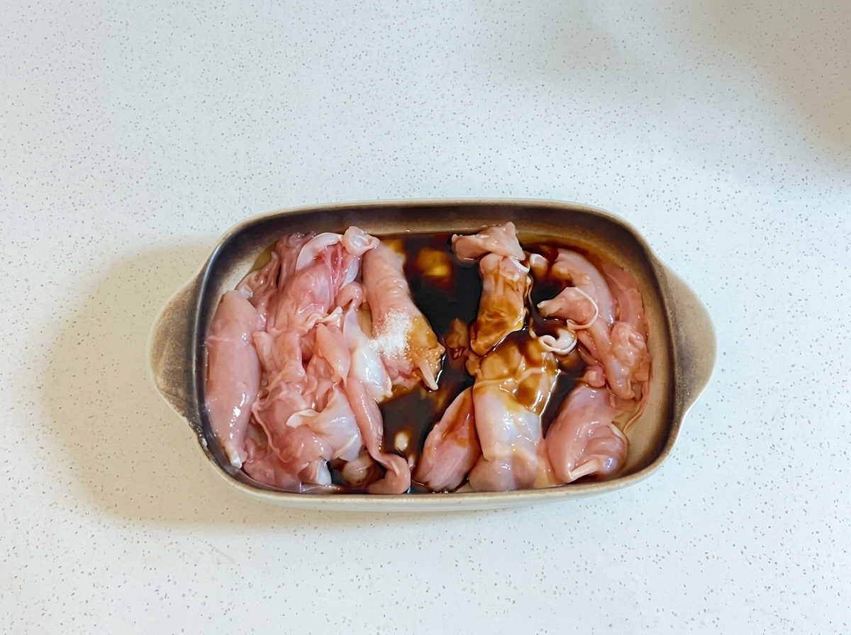 Des liquides de cuisson foncés et de lhuile versés sur des morceaux de poulet crus dans un plat de cuisson.