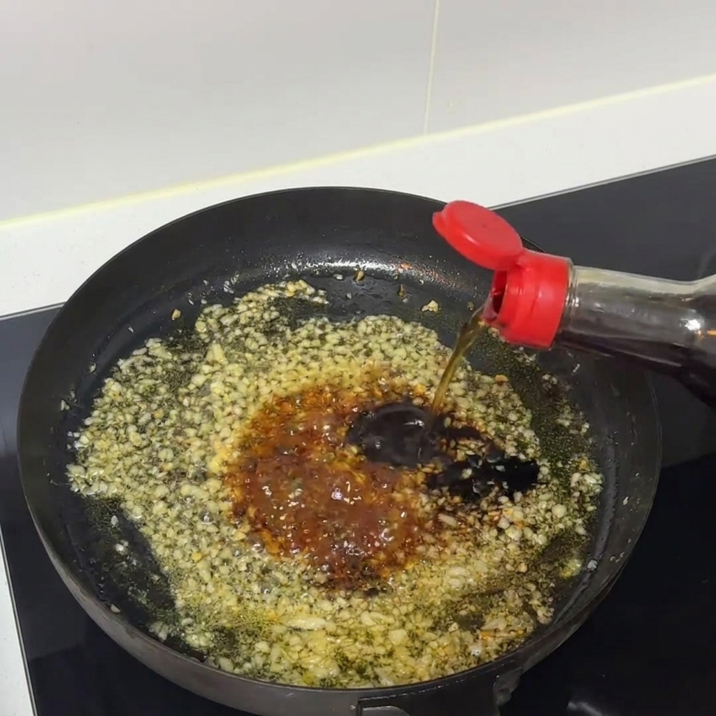 Un mélange de sauce sombre qui mijote et est remué à lintérieur dune poêle avec de lail haché.
