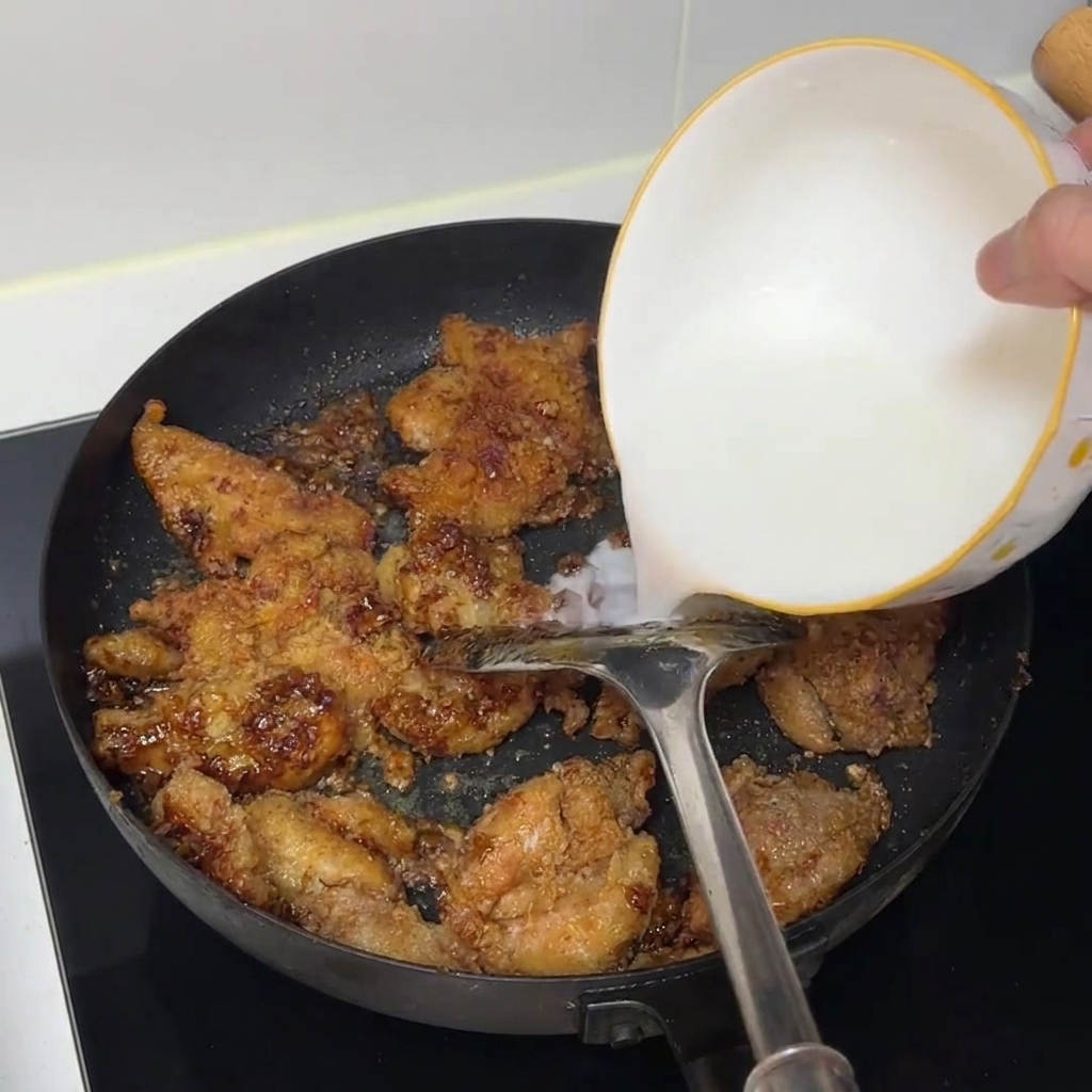 De leau de fécule versée dun bol blanc dans une poêle remplie de morceaux de poulet cuits.