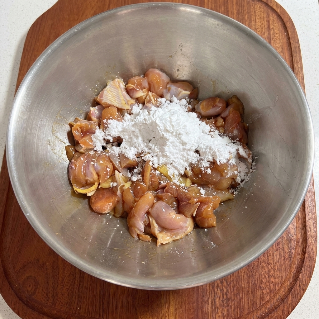 Une main mélangeant de la fécule blanche avec des morceaux de poulet assaisonnés à lintérieur dun bol en métal.