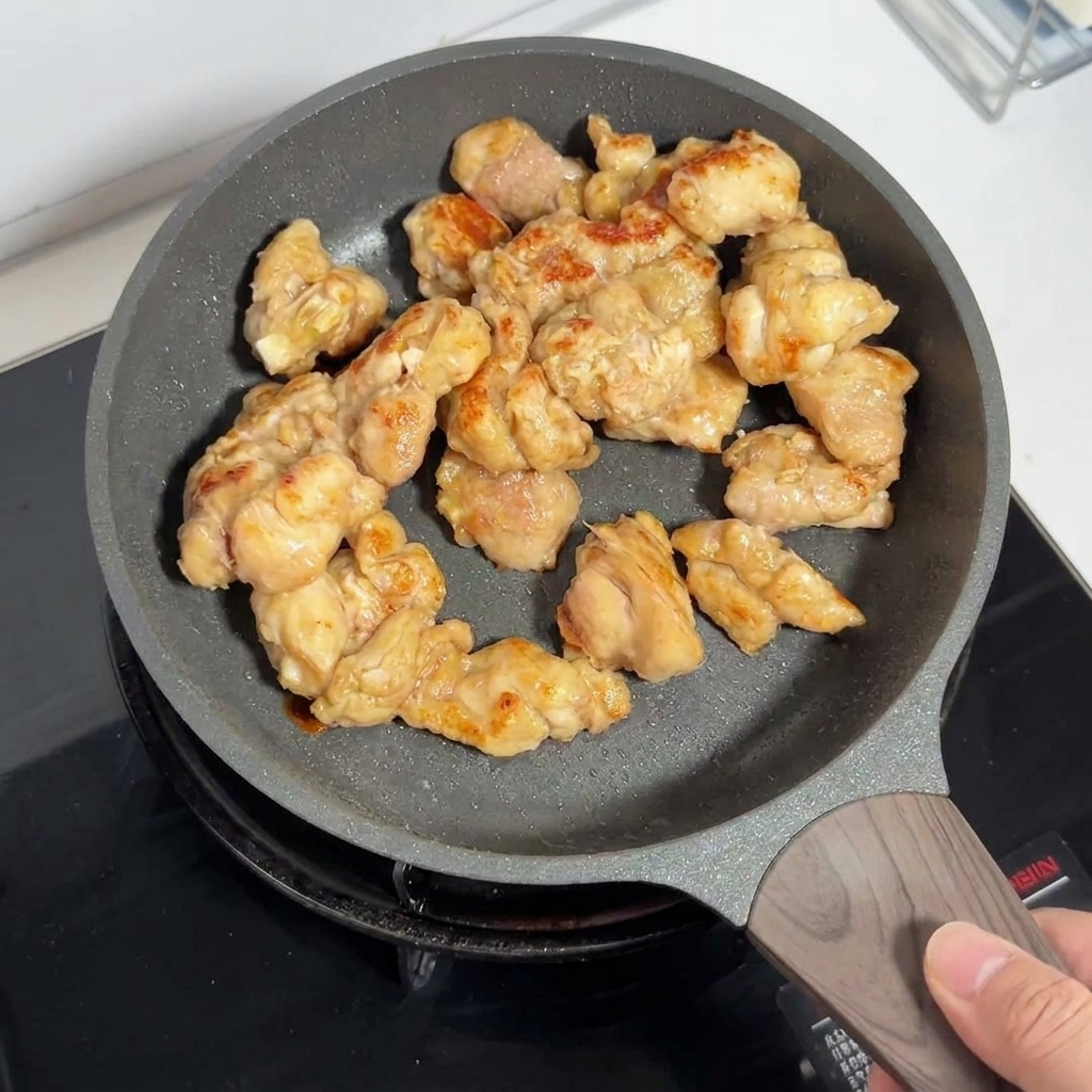 Morceaux de hauts de cuisse de poulet dorés en train de cuire dans une poêle antiadhésive.