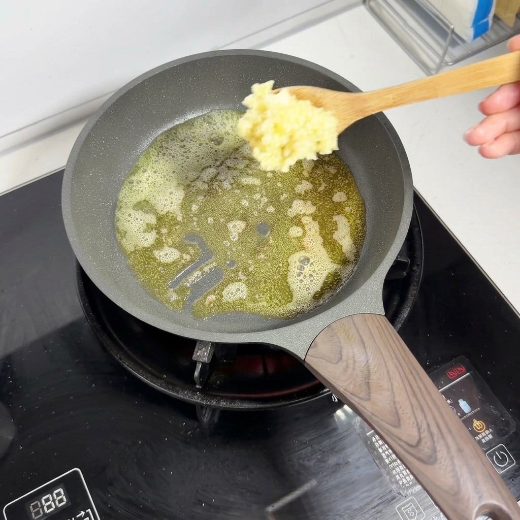 Une cuillère en bois ajoutant de lail haché dans du beurre moussant fondu dans une poêle.