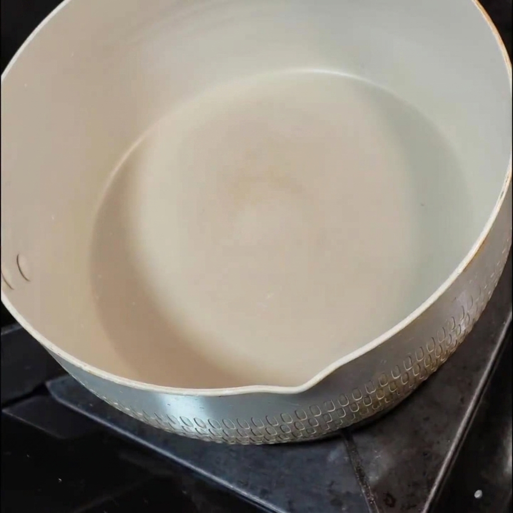 Une petite noisette de beurre fond dans une poêle en céramique blanche sur un feu de cuisinière.