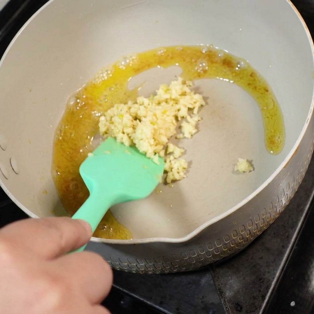 De lail frais émincé ajouté au beurre fondu dans une poêle, remué avec une spatule en silicone verte.