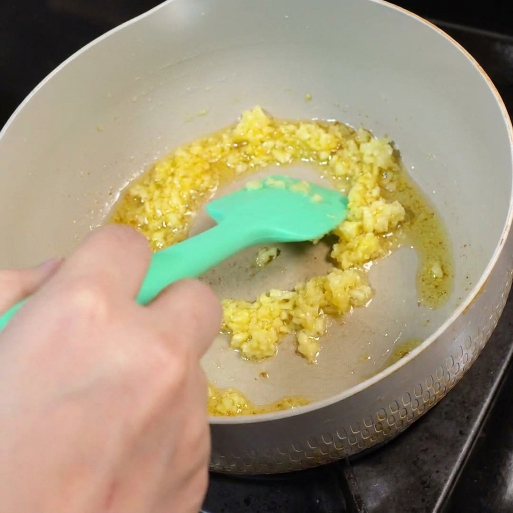 De lail émincé qui frit dans le beurre fondu dans une poêle, remué avec une spatule en silicone verte.