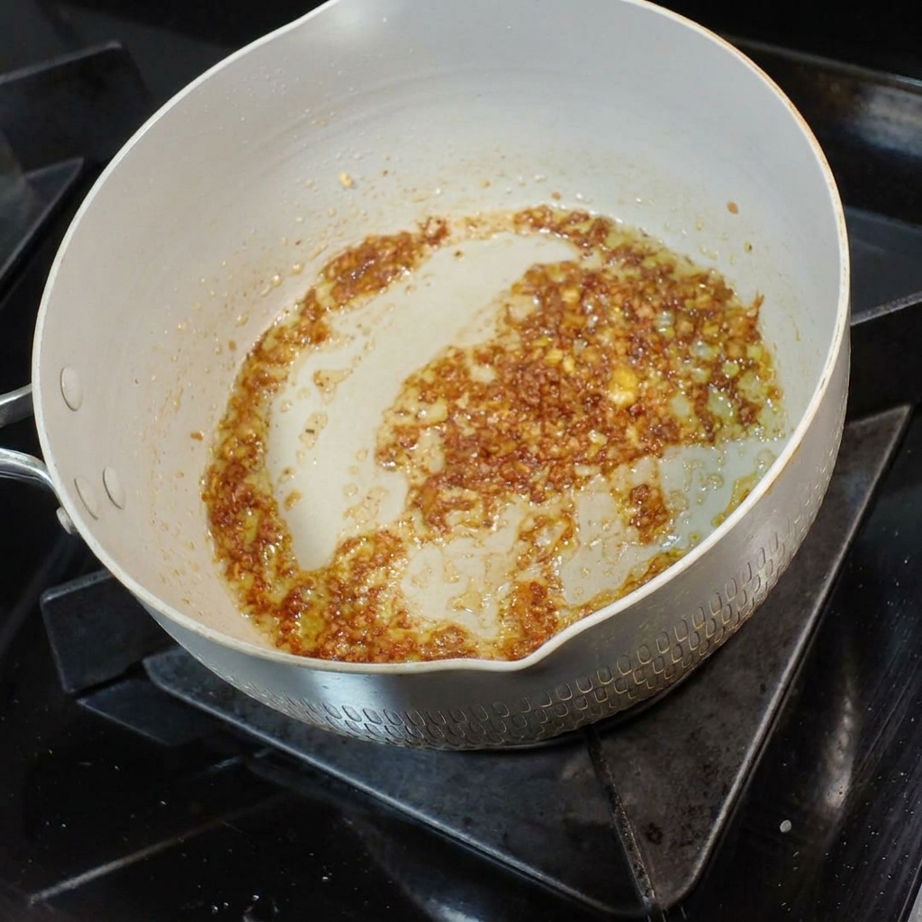 Une petite louche de bouillon de nouilles savoureux versée dans le mélange aromatique de beurre à lail.