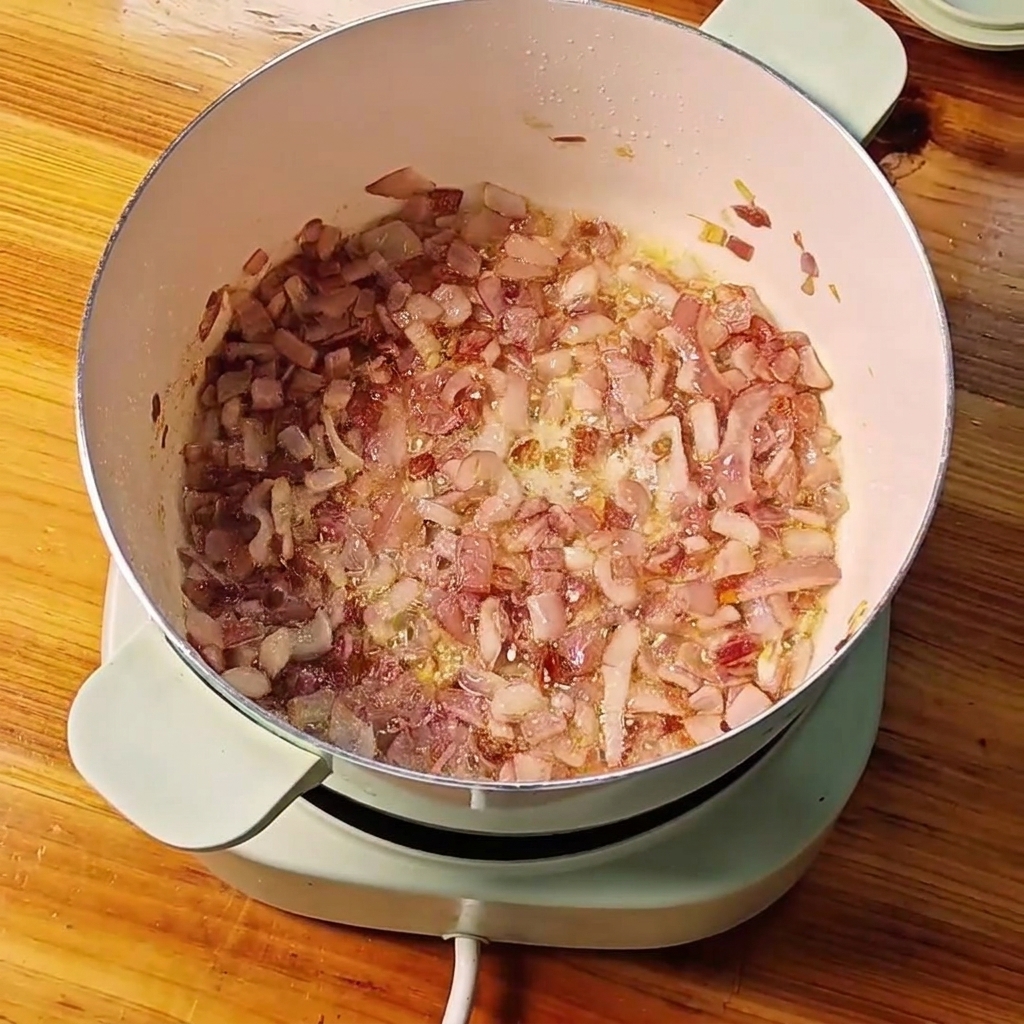 Oignons rouges en dés sautés dans une casserole avec de lail et du gingembre hachés en train dêtre mélangés.