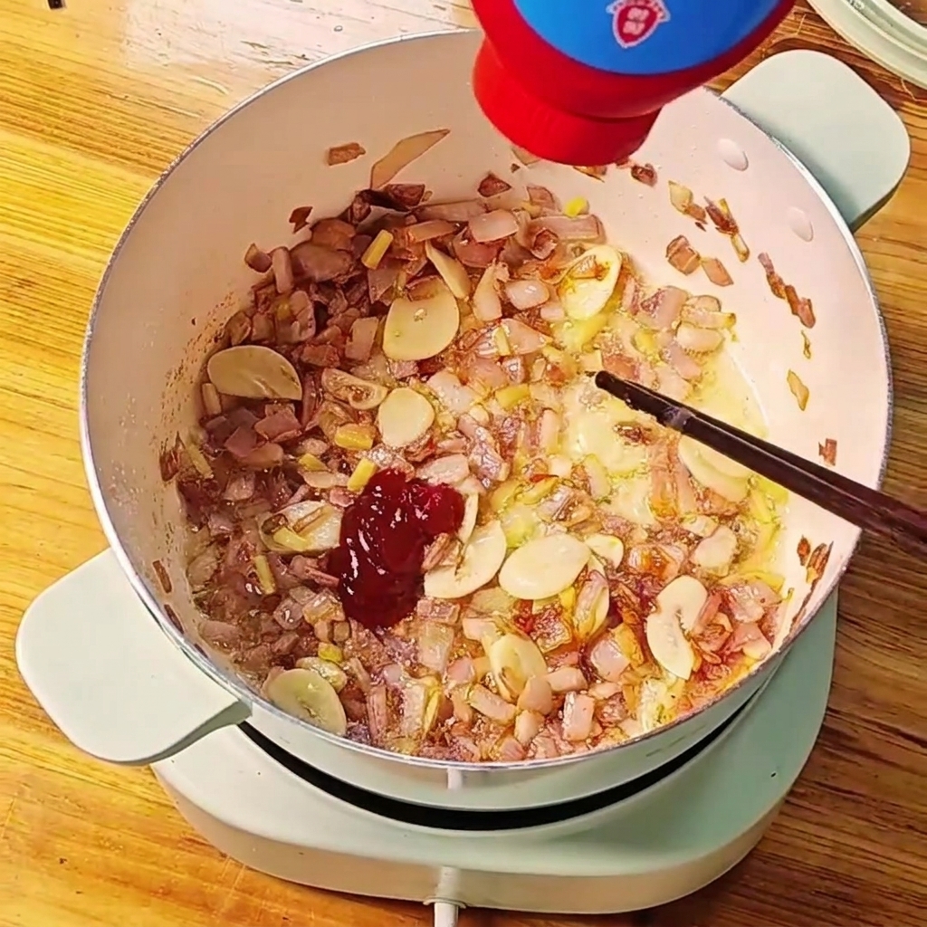 Concentré de tomate rouge pressé hors dun tube dans une casserole doignons et dail sautés.