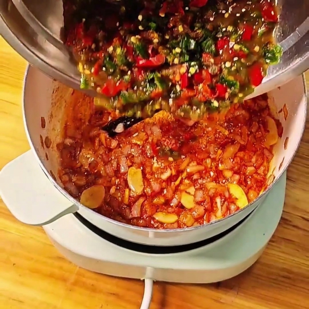 Mélange de tomates et de piments verts et rouges écrasés versé dun bol en métal dans la casserole.